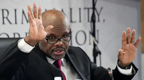 Gallo Images via Getty Images Police boss Shadrack Sibiya is seen with his hands up as he testifies at a public inquiry investigating police corruption