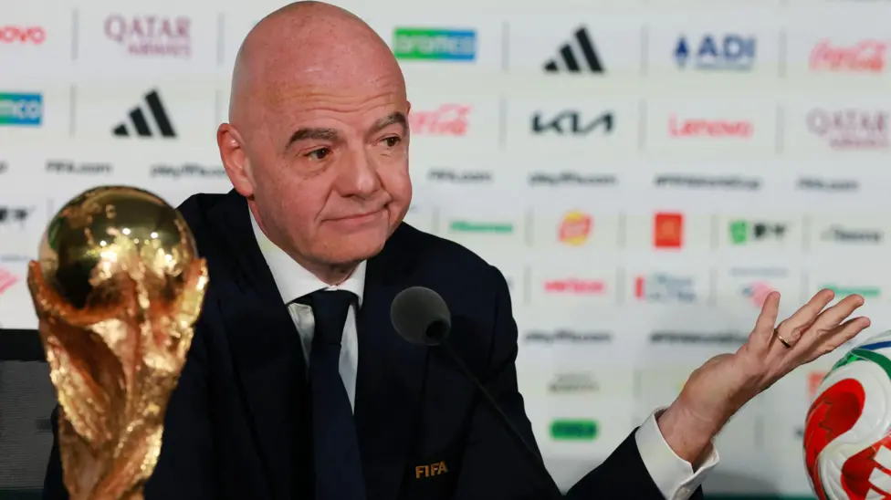 Fifa president Gianni Infantino sitting behind the gold World Cup trophy and shrugging