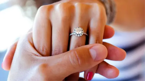 Getty Images A close up of a man holding a woman's hand with a diamond engagement ring
